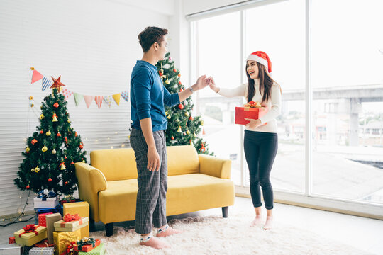 Romantic Asian couple in love, dancing together with a gift in woman hand and spending Christmas holiday together, woman and man enjoying good relationships in cozy home interior.