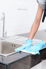Hands in blue gloves clean sink with sponge and a special cleaning agent, detergent spray. Hygiene in the kitchen, cleaning the kitchen, household. Hand squeezes sponge and sprays drops of water.