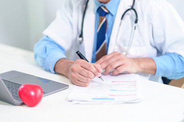Senior doctor physician using laptop, writing prescription with stethoscope on desk. Old male professional therapist wearing white coat working in hospital. Healthcare, medicine concept. Close up view