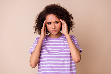 Photo of depressed tired girl dressed purple t-shirt arms temples looking empty space isolated beige color background