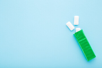 Opened green pack with white chewing gum pads on light blue table background. Pastel color....