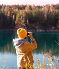 Young woman in yellow hat looking through binoculars at birds on lake against autumn forest Birdwatching, zoology, ecology. Research in nature, observation of animals Ornithology