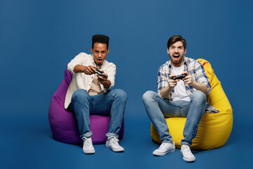 Full body young two friend men wear white casual shirts together looking camera hold in hand play pc game with joystick console isolated plain dark royal navy blue background People lifestyle concept