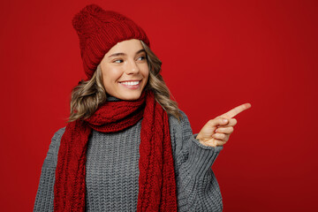 Young woman wear warm grey sweater scarf hat point index finger aside on workspace area mockup isolated on plain red background studio Healthy lifestyle ill sick disease treatment cold season concept