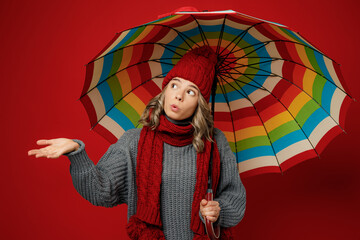 Young woman wear grey sweater scarf hat hold opened colorful umbrella catch raindrops isolated on...