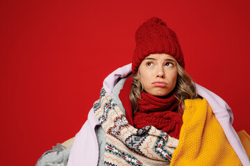 Young frozen sad woman wear scarf hat wrapped in many plaids look overhead on area isolated on plain red background studio portrait. Healthy lifestyle ill sick disease treatment cold season concept.
