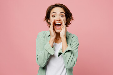 Young happy fun promoter woman 20s she wear green shirt white t-shirt scream sharing hot news about sales discount with hands near mouth isolated on plain pastel light pink background studio portrait.