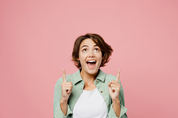 Young surprised shocked cool woman 20s wear green shirt white t-shirt point index finger overhead...