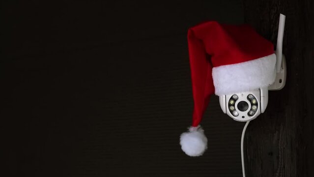 White CCTV camera says yes in red Santa Claus hat rotates and records moving objects. Fun humor. Outdoor video surveillance. Web cam. Security system. Distance street control. Smart tech. Copy space.