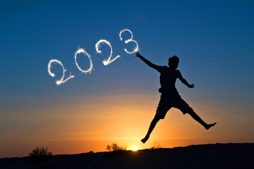 2023 written with sparkles, silhouette of a boy jumping in the sun, new year card