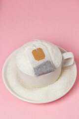 Tea with a lot of added sugar. Cup overflowing with sugar and tea bag on pink background