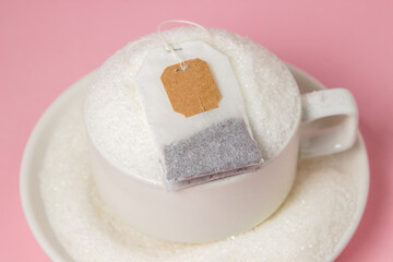 Tea with a lot of added sugar. Cup overflowing with sugar and tea bag on pink background