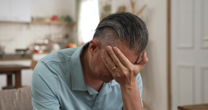 front view thoughtful middle aged mature grandfather sitting on couch. Pondering old senior hoary man thinking of psychological health problems spending time alone at home.