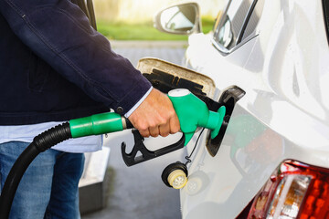 Man holding gasoline fuel nozzle to refuel benzine gas into vehicle petrol station, day light. Transportation and ownership concept. 