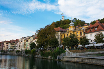 Fototapeta na wymiar Historic buildings on the waterfront of the Ljubljanici River in central Ljubljana, Slovenia. The castle tower is seen on Castle Hill on the background 