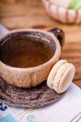 Ceramic cup with tea and coffee macaron on a wooden table