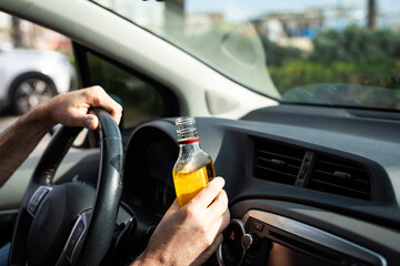Driver driving a car with a bottle of alcohol in his hands close-up.