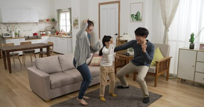 Full Length Shot Happy Asian Family Of Three Having Fun Dancing Together At Home. They Move Their Body To Song In A Cozy Modern Home Interior With Daylight