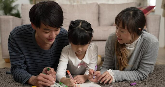 cheerful chinese family of three having fun lying prone on living room floor drawing picture together. family love and happy childhood concept