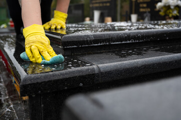 Headstone cleaning on cemetery. Professional in yellow gloves cleans the marble grave, scrubbing with sponge and water. Tombstone preparation for All Saints Day on November 1st