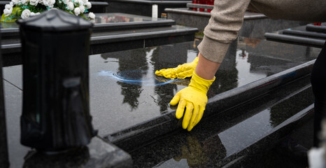 Headstone cleaning on cemetery. Professional in yellow gloves cleans the marble grave, polishing...