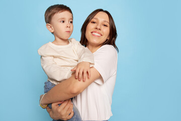 happy young woman and little boy, mother hugging her son isolated on blue studio background. Mother's Day celebration. Concept of family, childhood, motherhood