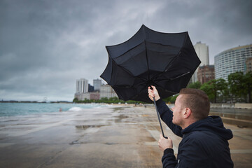 Man holding broken umbrella in strong wind during gloomy rainy day in city..