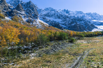 Panorama with mountain view. View of the mountain peaks. Snow in the mountains. Nature in the mountains. Snow-capped mountain peaks. The multi colored color of trees in autumn in a mountainous area.