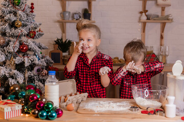  children in red plaid pajamas play with flour in the Christmas kitchen. homemade baking. lifestyle