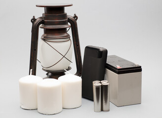 oil lamp, power bank with batteries, white candles and battery with connection bolts gray background