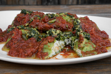 Pasta. Closeup view of spinach ravioli with tomato sauce and pesto, in a white dish on the wooden table.