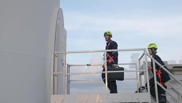 In the evening, Two maintenance engineers in safety gear working at height stood talking after doing repair, check and maintenance work. Wind turbines complete power generation , clean energy concept,