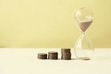 hourglass and stack of coins on table, 