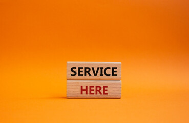 Service here symbol. Concept words Service here on wooden blocks. Beautiful orange background. Business and Service here concept. Copy space.