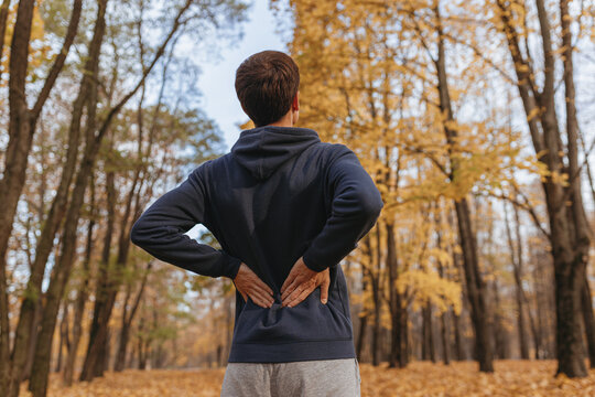 Low angle of sportsman stretching back while doing exercise in autumn park and training outdoors 