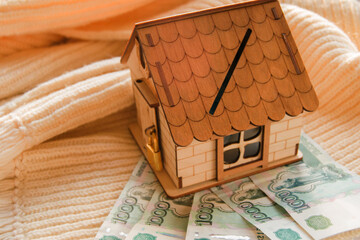 Close-up of a model of a wooden house on a warm scarf with money and keys. the concept of saving for a warm new home