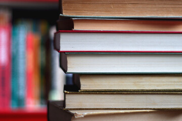 Stack of colorful hardcover books and reading glasses in front of a bookshelf. Selective focus.