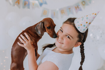 little girl in a white dress with her beloved dog dachshund in her arms celebrates her birthday