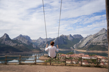 Blonde woman swinging on a giant wooden swing, in front of the amazing mountainous landscape of the...