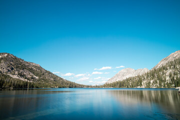 Toxaway Lake, located in Idaho’s Sawtooth Wilderness seen on a summer day, with a blues sky, white clouds and a reflection in the calm waters of the pristine alpine lake.