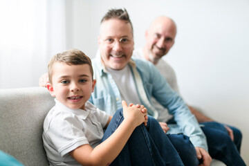 Happy two man couple with adopted child sit on sofa at home