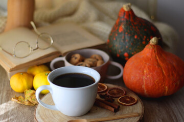Cup of tea or coffee, seasonal spices, bowl of cookies, blanket, pumpkins, colorful leaves, books and tangerines on wooden table. Cozy hygge at home. Selective focus.