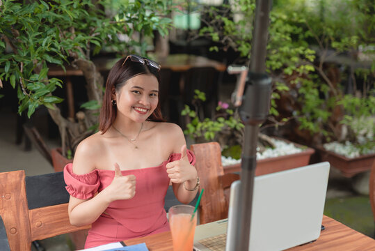 A female non-voice call center agent dining in an al fresco cafe holds a thumbs up as she approves of the work from home setup.