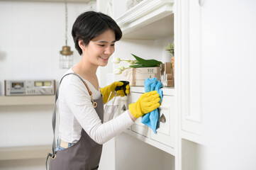 An Asian woman with cleaning gloves using alcohol spray sanitiser to cleaning house, healthy lifestyle concept.