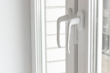 White plastic window handles detail, closeup view, horizontal photo. Closed modern windows in flat, PVC plastic, handles turned down side view, cold weather