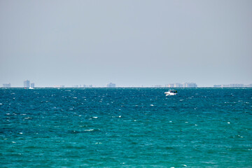 Sea panorama. Small motor boat floats in deap blue bay water under bright blue sky, tall buildings on distant shore