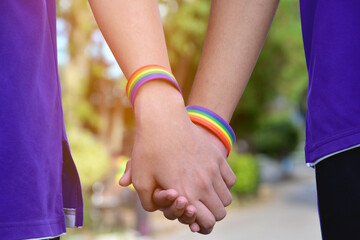 Rainbow wristband wearing in hand of young asian gay to show and represent gender diversity, to respect human rights in alternative sex, to stop punishing homosexuals in some religions. - obrazy, fototapety, plakaty
