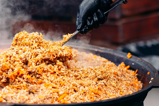 Chef cook prepares Yellow pilaf in cauldron with beef from street food market at festival