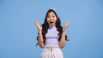 amazed and young asian woman with opened mouth gesturing isolated on blue