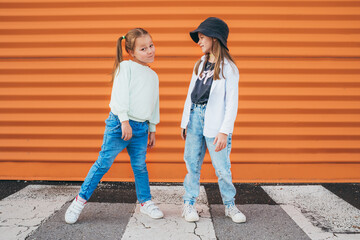 Two little girls sisters dressed kids fashion vogue style clothes posing at camera on the city...